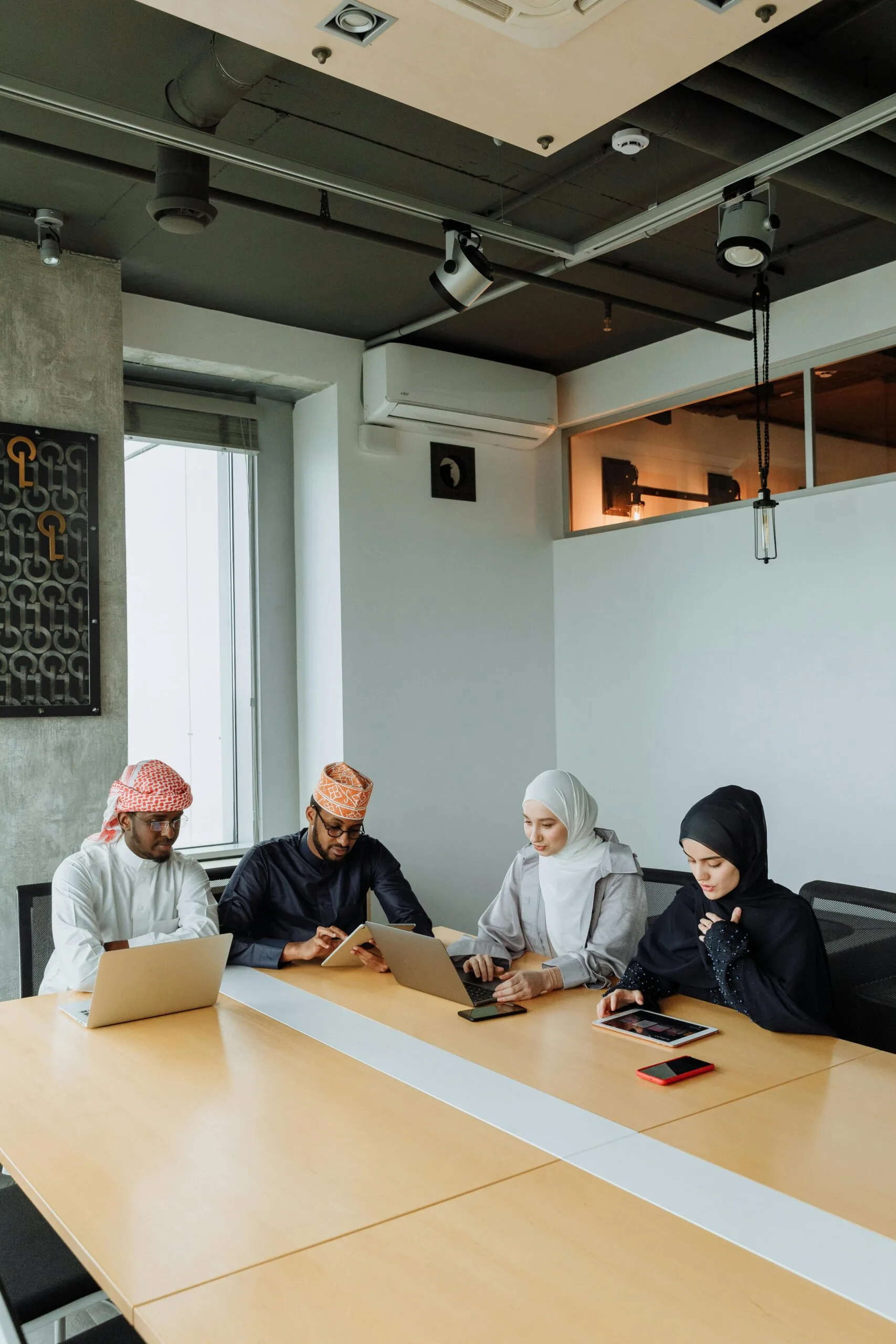 pexels-photo-7984737-7984737-3 A group of Muslim professionals collaborating in a modern meeting room with laptops and tablets.