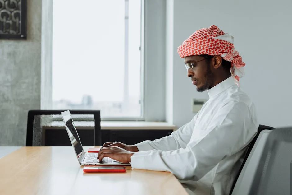 pexels-photo-7984742-7984742-1 Middle Eastern man focused on work at a modern office desk with a laptop.