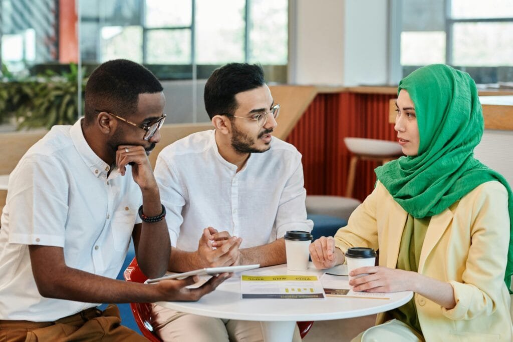 Three diverse colleagues in a modern office having a focused conversation around a table.